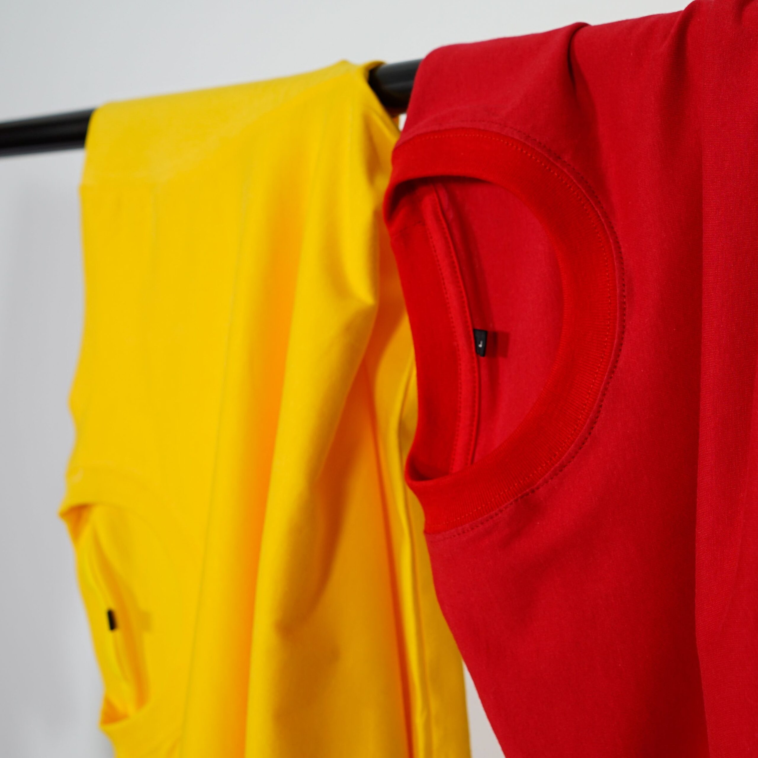 Red and yellow t-shirts neatly hanging indoors on a black clothing rack.